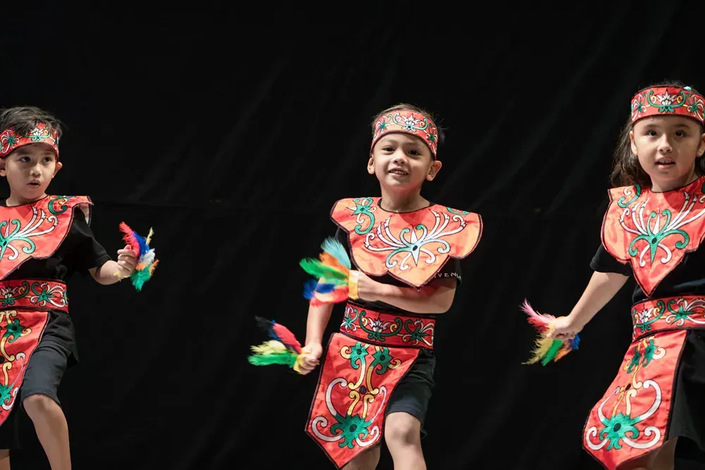 Three children are dancing in traditional costumes on a stage.