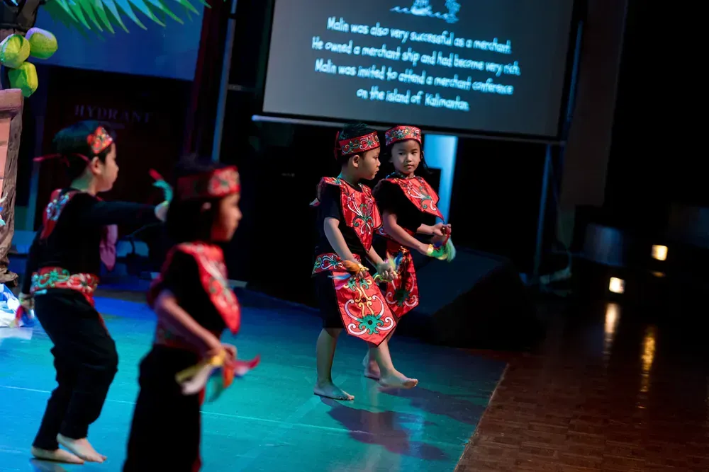 A group of children are dancing on a stage in front of a projector screen.