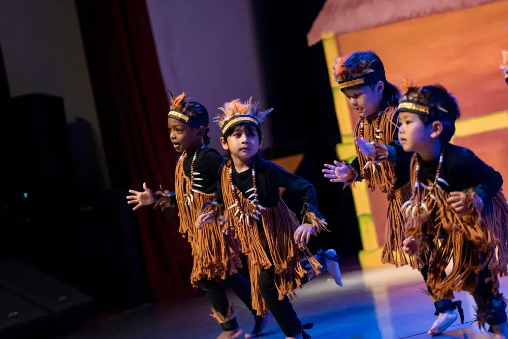 A group of children in native american costumes are dancing on a stage.