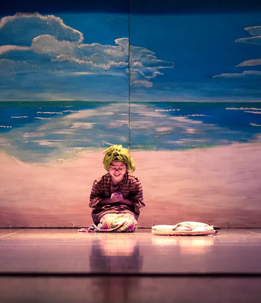 A person is sitting on the floor in front of a painting of a beach.
