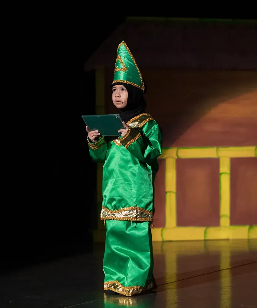 A little girl in a green costume is holding a tablet