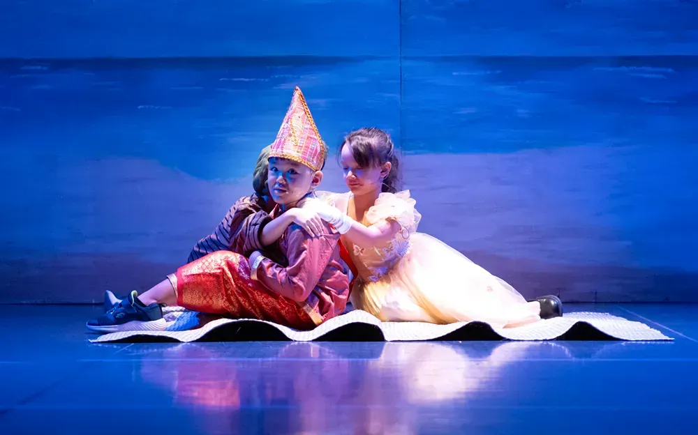 A boy and a girl are sitting on a carpet on a stage.