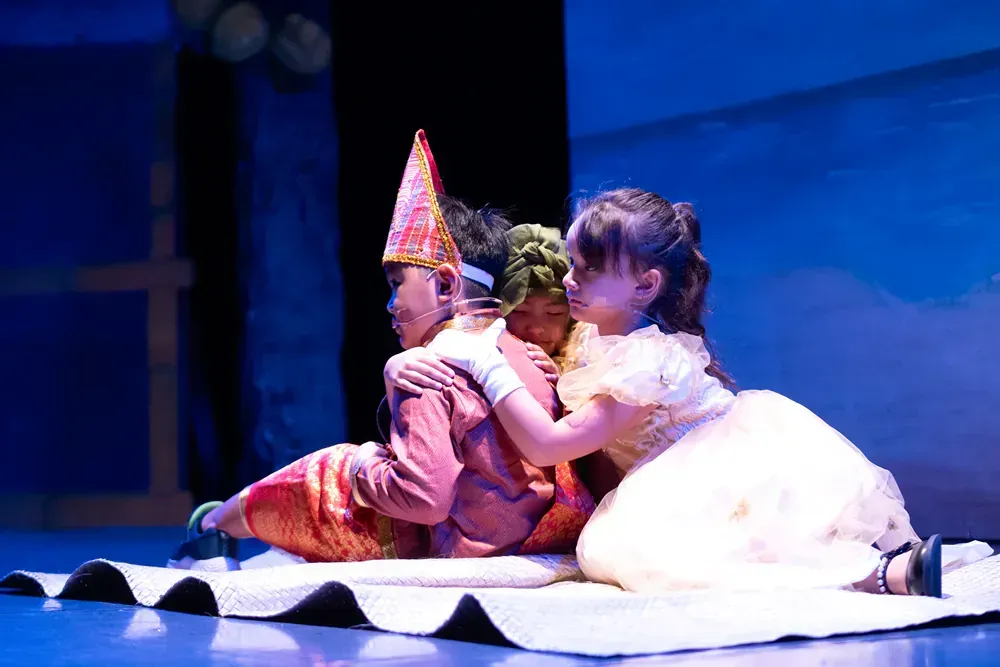 A boy and a girl are laying on a blanket on a stage.