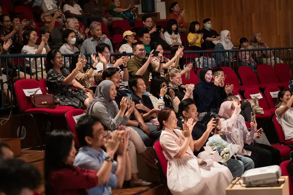 A large group of people are sitting in a theater applauding.