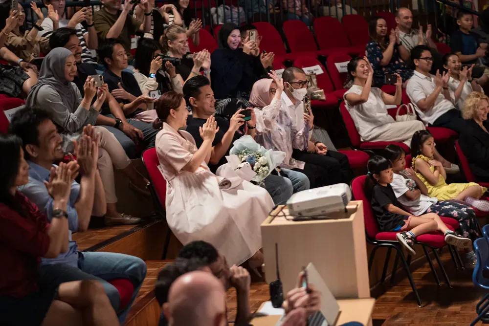 A large group of people are sitting in a theater applauding.