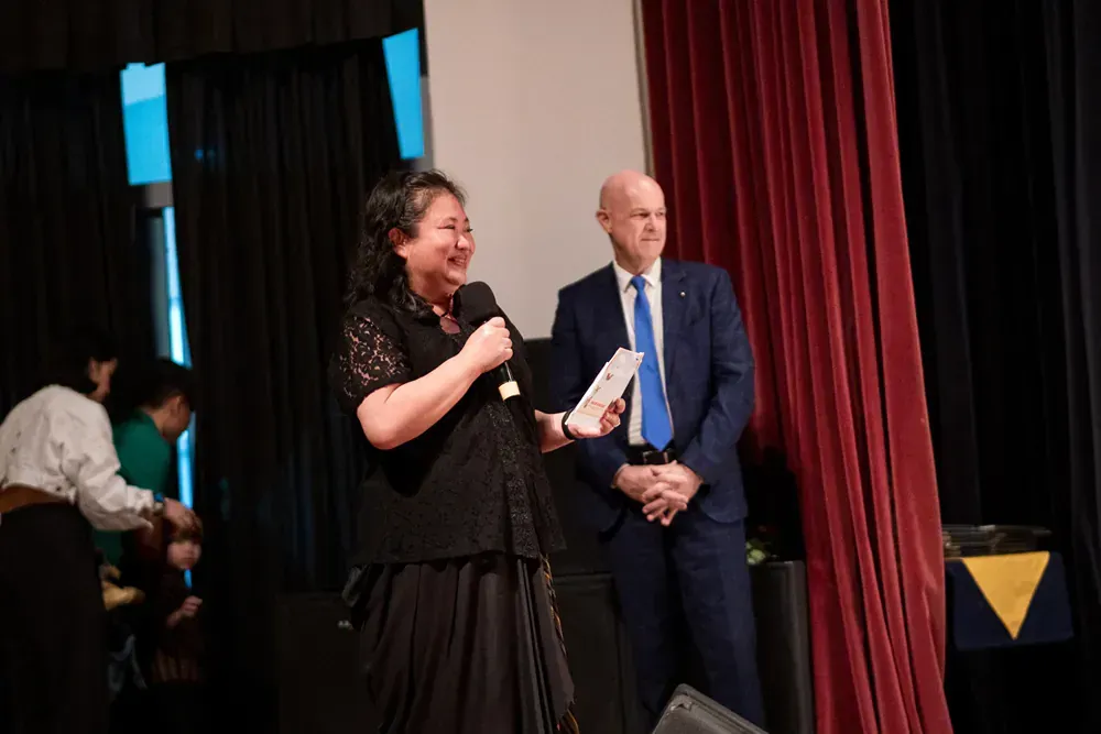A woman is speaking into a microphone while standing next to a man in a suit on a stage.