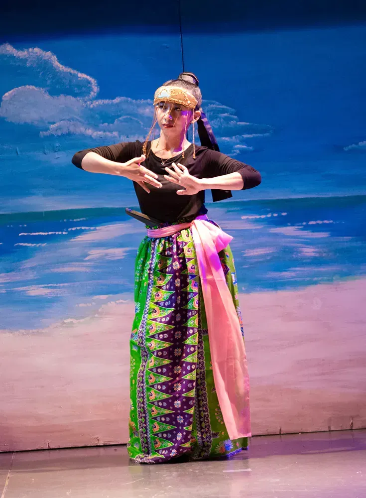 A woman in a green and pink skirt is dancing on a stage.