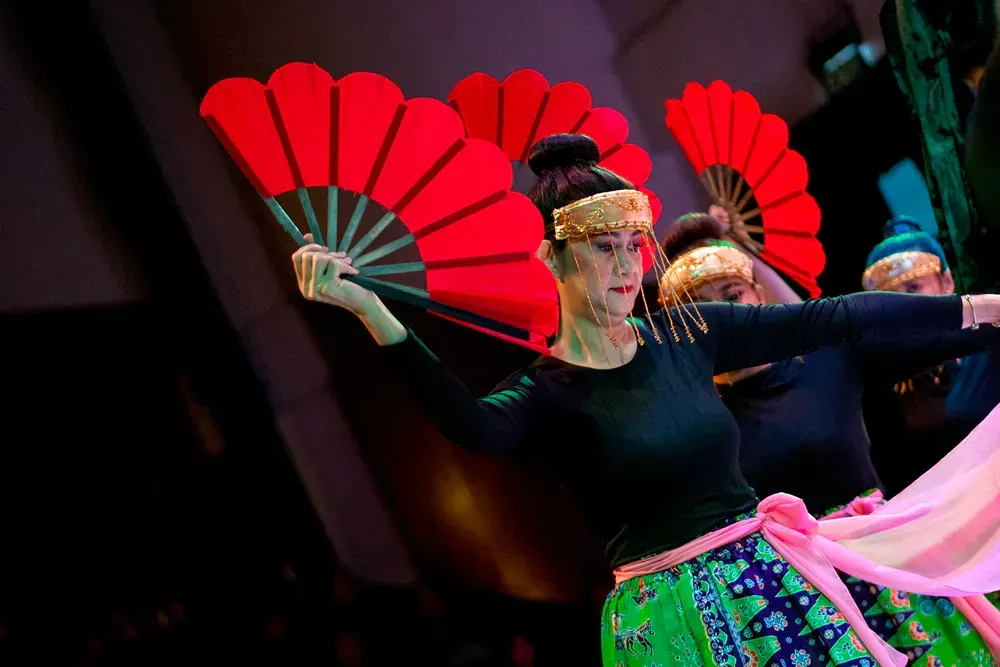 A group of women are dancing with red fans in a dark room.