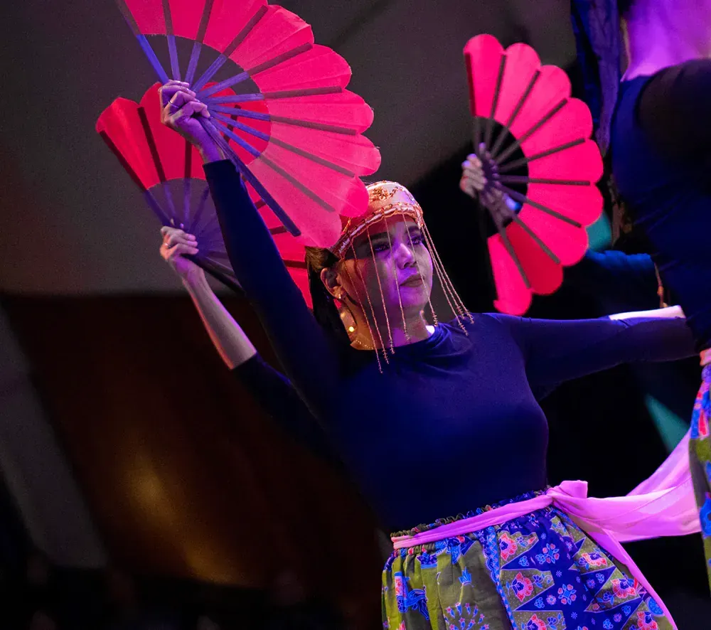 A woman in a blue top is holding two pink fans