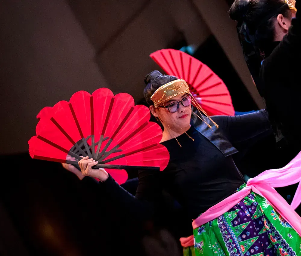A woman is holding two red fans in her hands.