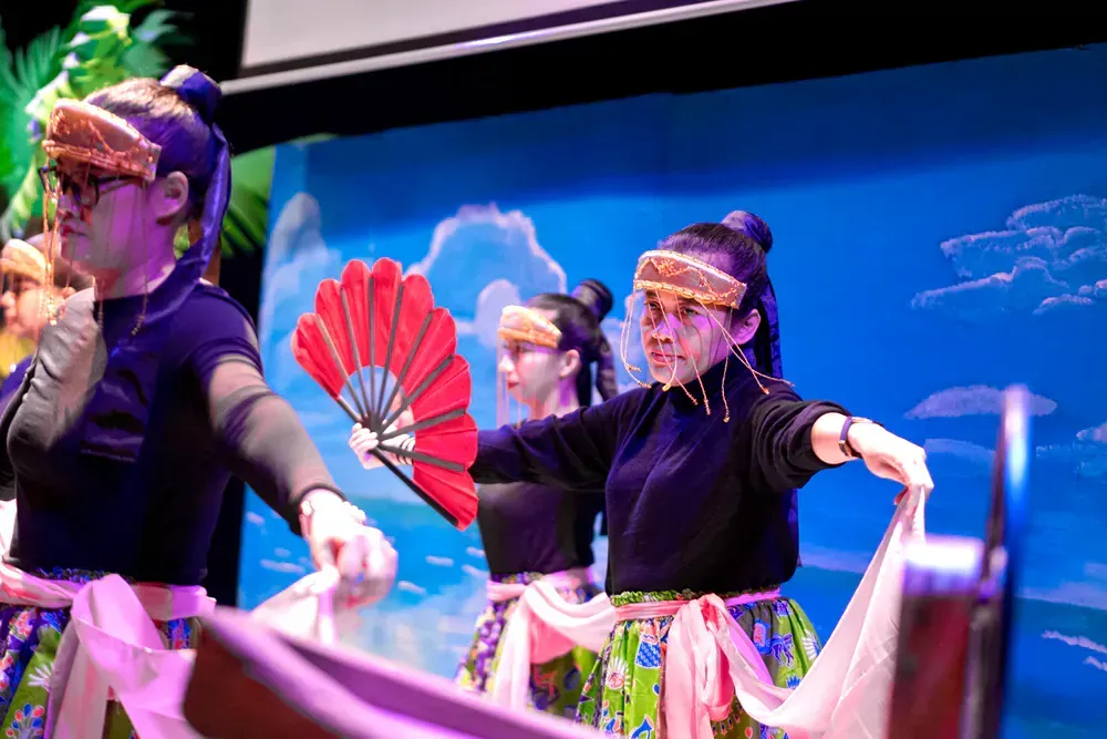 A group of women are dancing on a stage while holding fans.