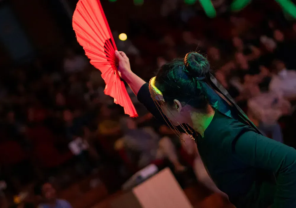 A woman is holding a red fan in front of a crowd.