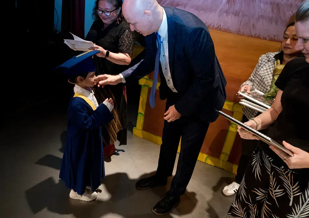 A man in a suit is shaking hands with a young boy in a graduation cap and gown.