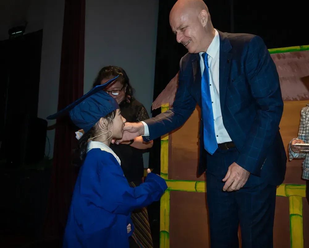 A man in a suit and tie is shaking hands with a little girl in a graduation cap and gown