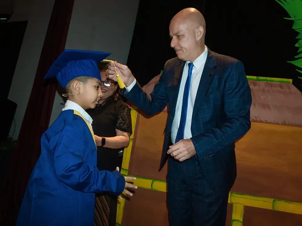 A man in a suit and tie is giving a diploma to a young boy in a graduation cap and gown.