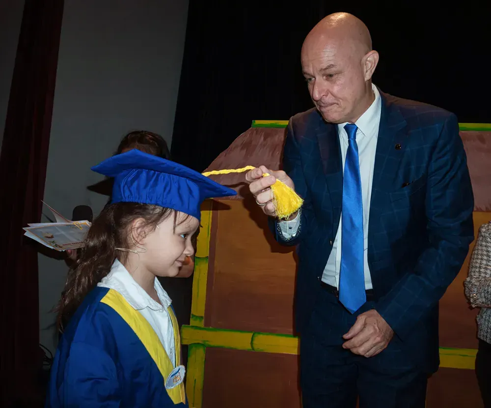 A man in a suit and tie is holding a yellow object next to a little girl in a graduation cap and gown