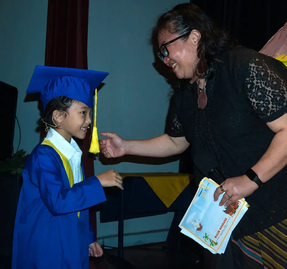 A girl in a graduation cap and gown shakes hands with a woman