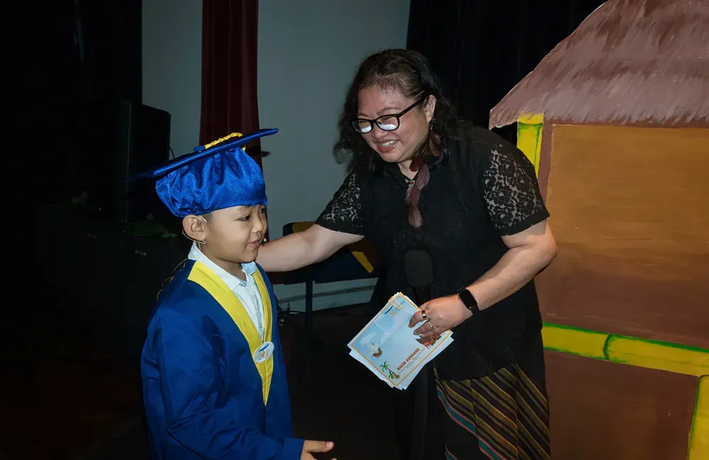 A woman is shaking hands with a young boy wearing a graduation cap and gown.