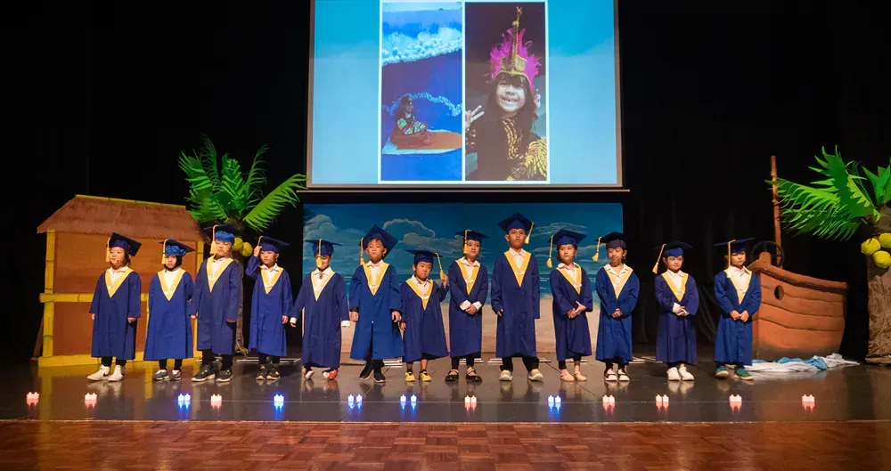 A group of children in graduation caps and gowns are standing on a stage.