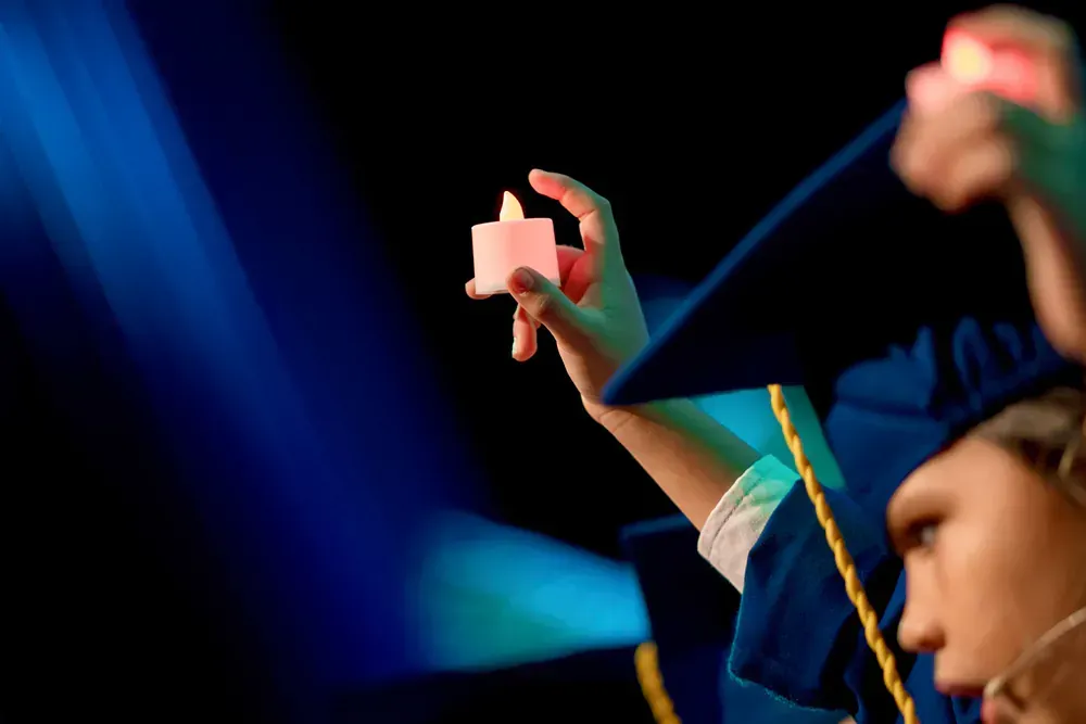 A woman in a graduation cap and gown is holding a candle in her hand.