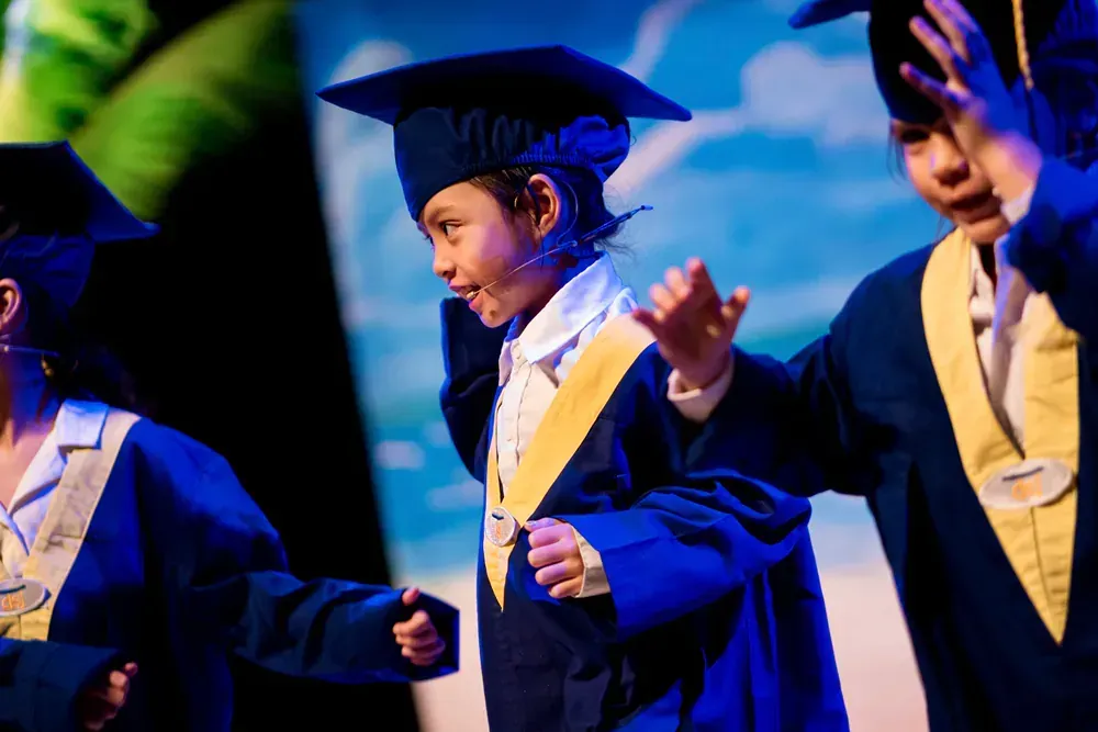 A group of children wearing graduation caps and gowns are dancing on a stage.