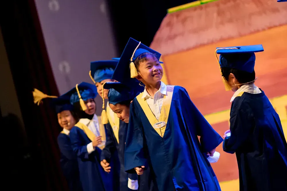 A group of children in graduation gowns and caps are standing on a stage.