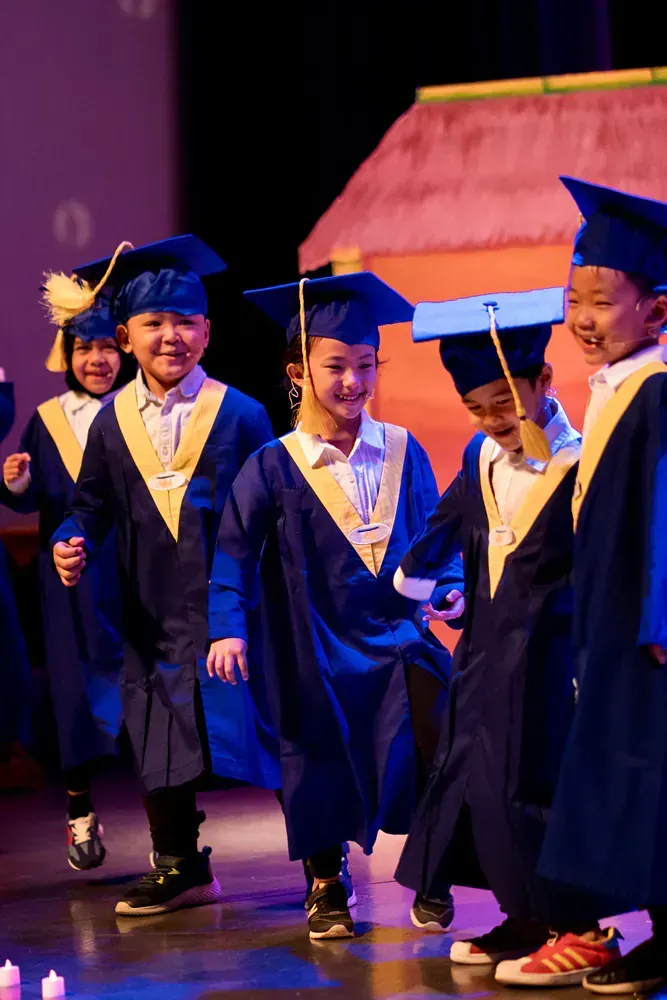A group of children wearing graduation caps and gowns are walking on a stage.