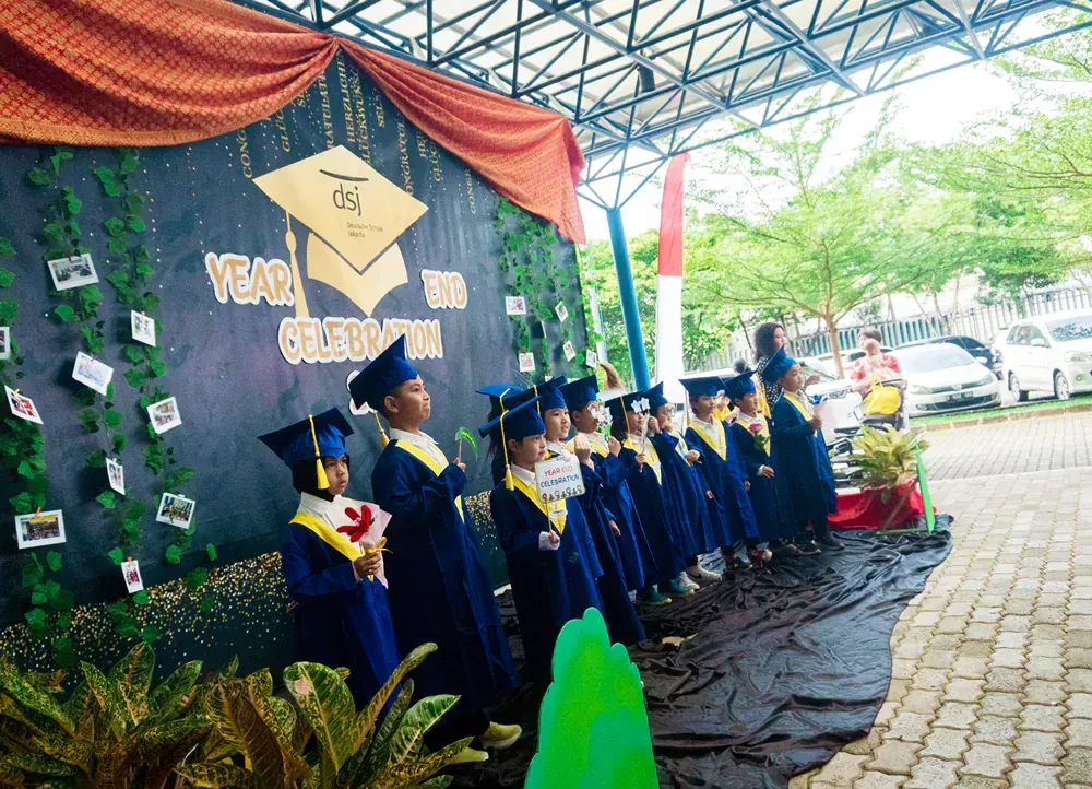 A group of children in graduation caps and gowns are standing in front of a sign that says year of graduation