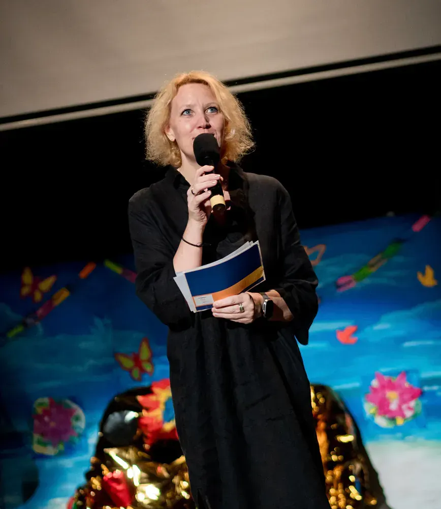 A woman in a black dress is speaking into a microphone