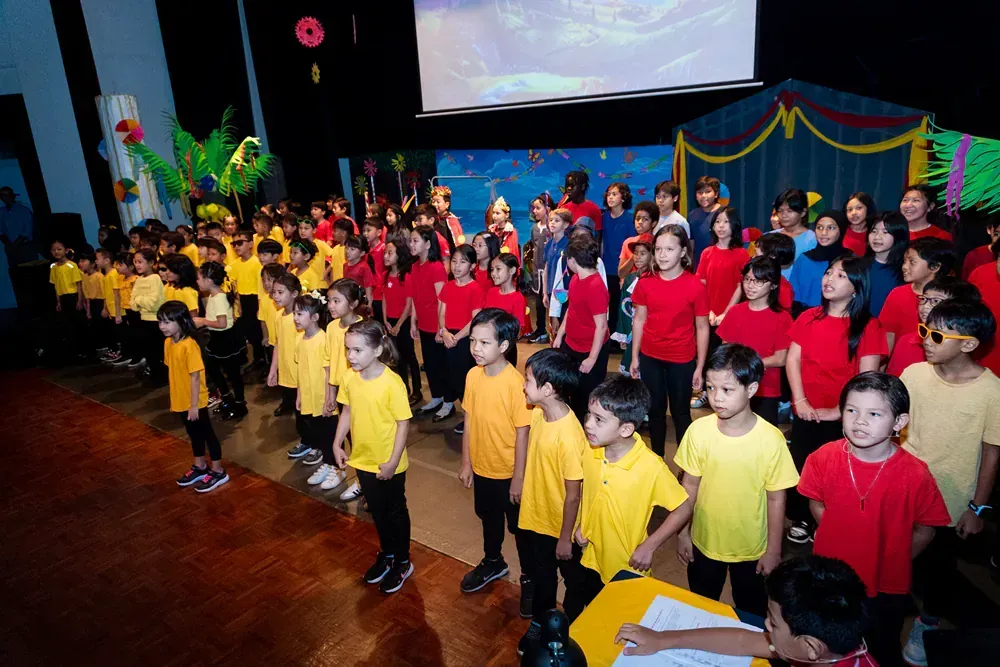 A large group of children in yellow shirts are standing on a stage.
