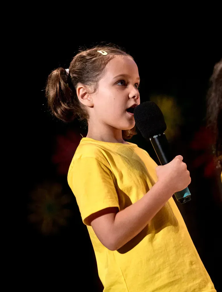 A little girl in a yellow shirt is singing into a microphone