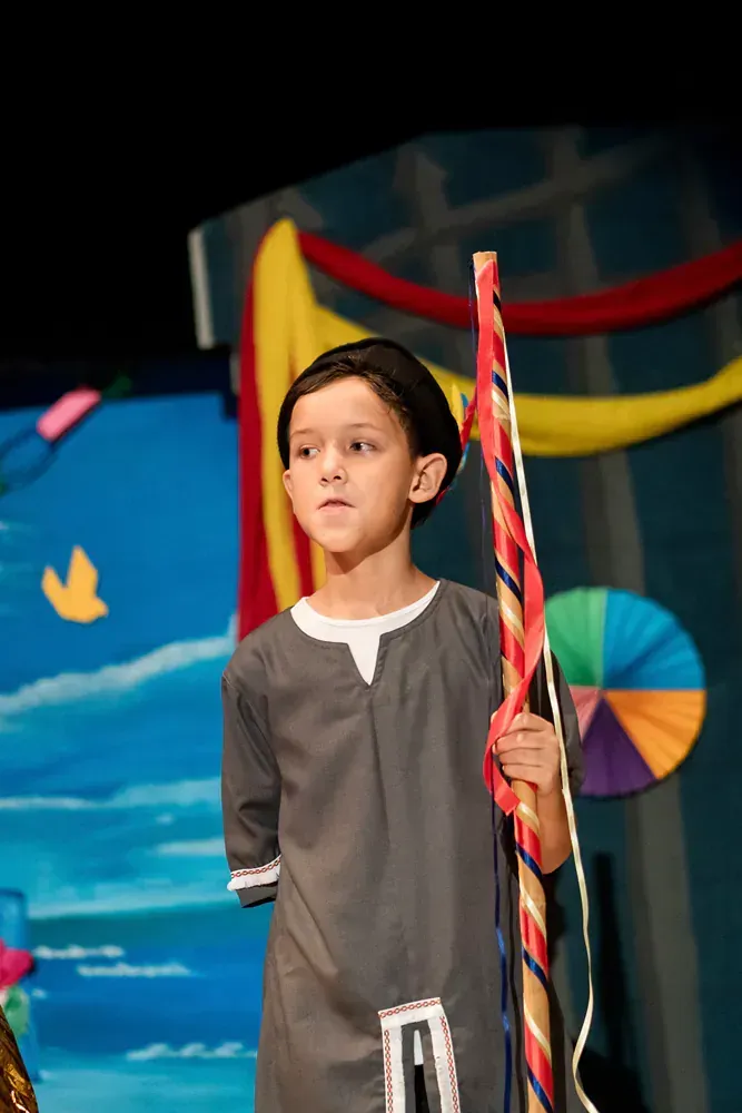 A young boy is holding a colorful stick on a stage.