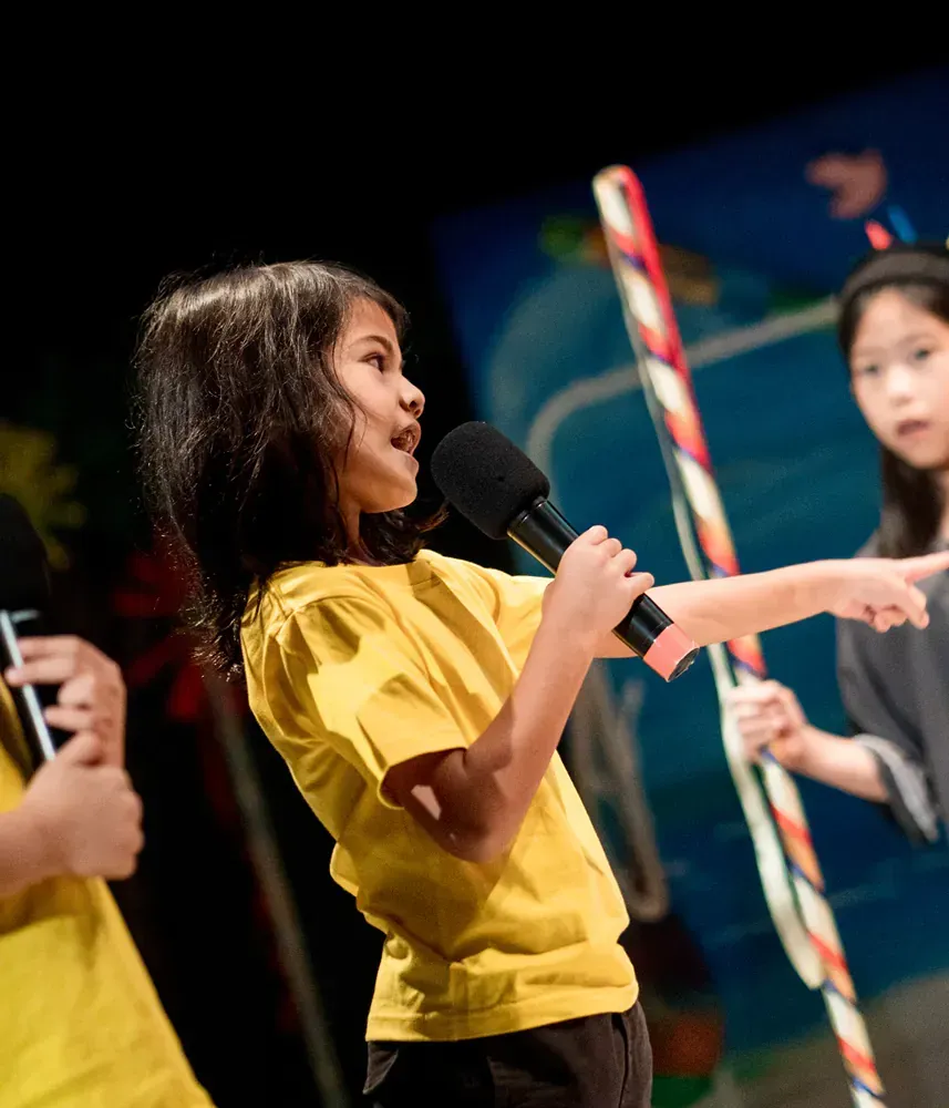 A little girl in a yellow shirt is holding a microphone