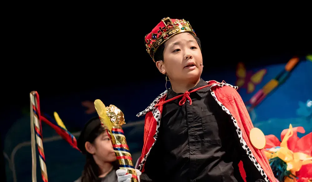 A young boy is wearing a crown and a red cape.