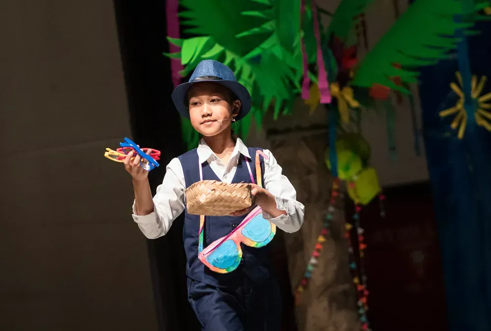 A young boy is standing on a stage wearing a hat and sunglasses.