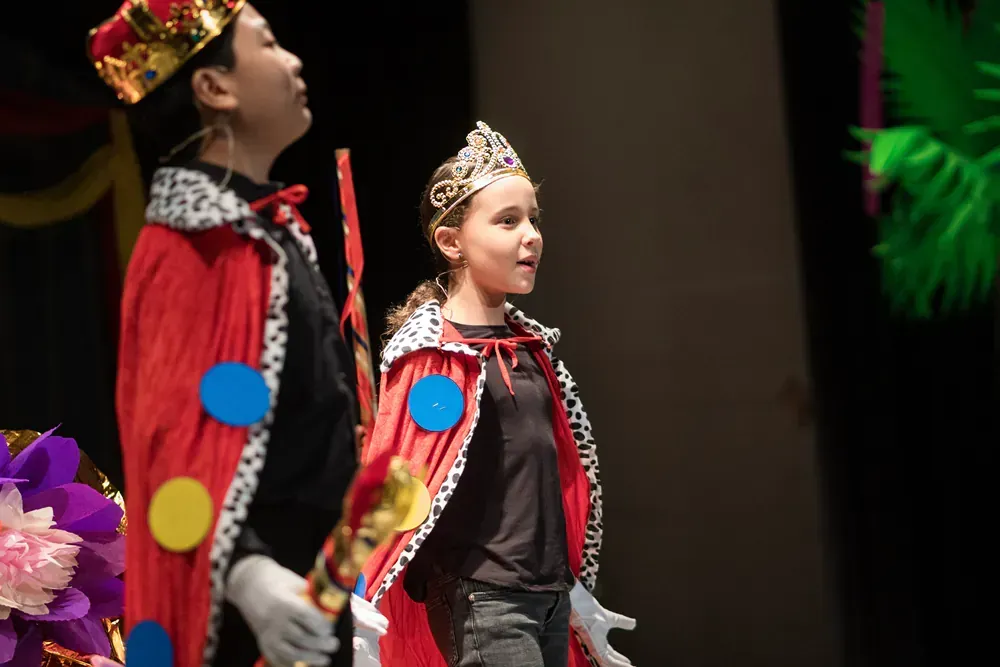 A boy and a girl are dressed up as kings and queens on a stage.