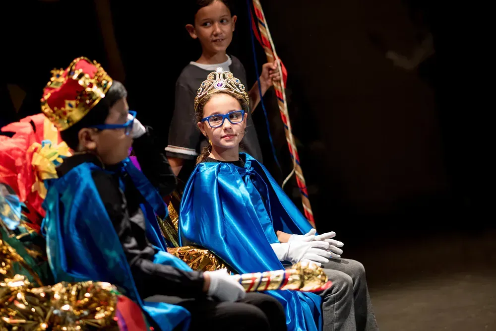 A group of children dressed in costumes are sitting on a stage.