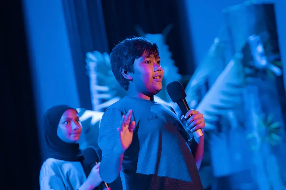 A young boy is holding a microphone on a stage.