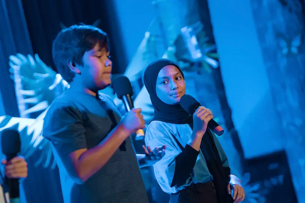 A boy and a girl are singing into microphones on a stage.