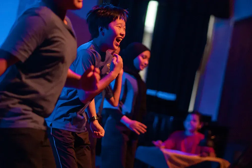 A group of children are dancing on a stage in a dark room.
