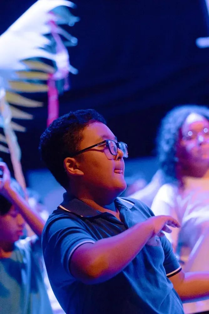 A boy wearing glasses and a blue shirt is dancing on a stage.