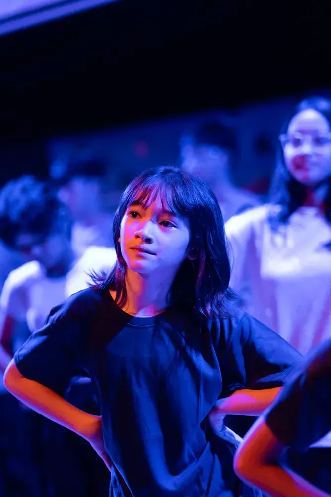 A group of young people are dancing on a stage in a dark room.