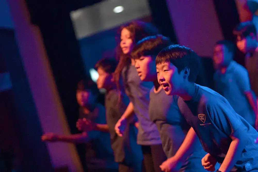 A group of children are dancing on a stage in a dark room.