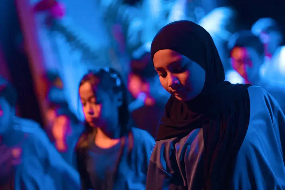 A woman in a hijab is dancing in a dark room.