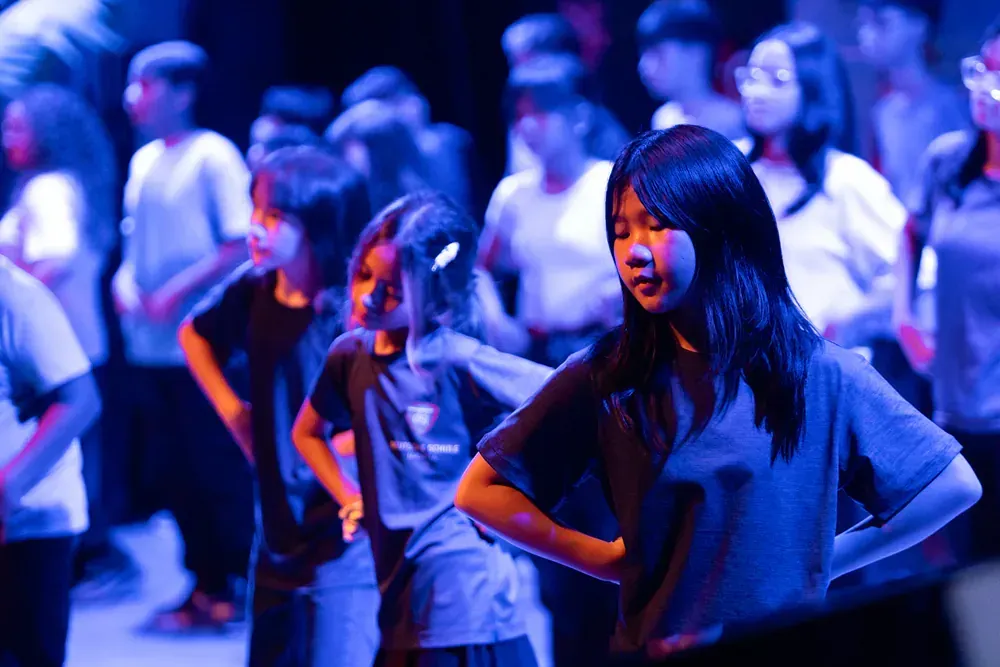 A group of young people are dancing on a stage in a dark room.