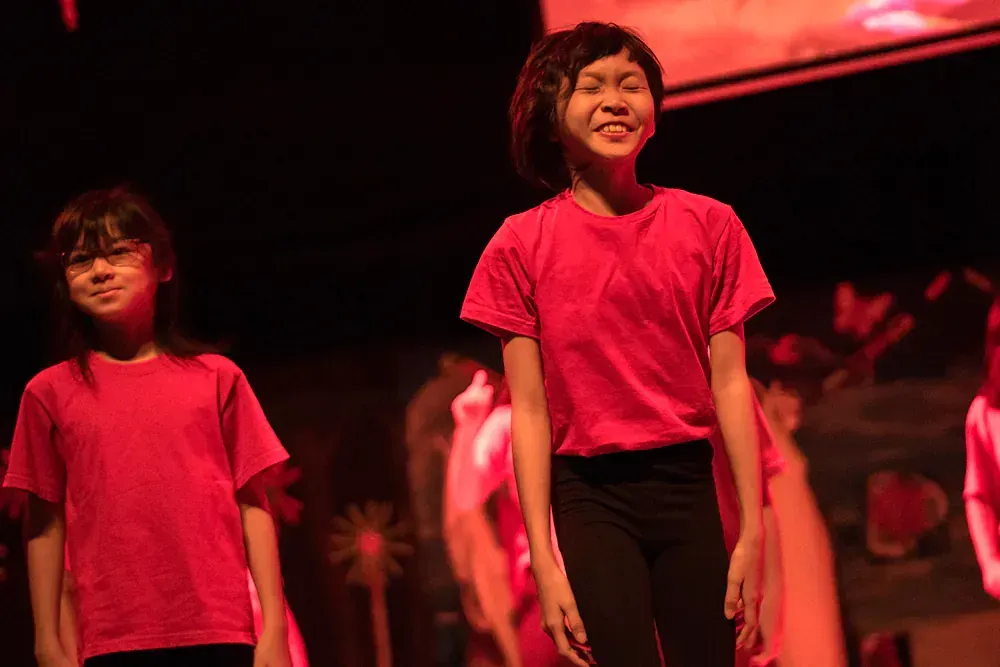 A group of young girls in red shirts are dancing on a stage.