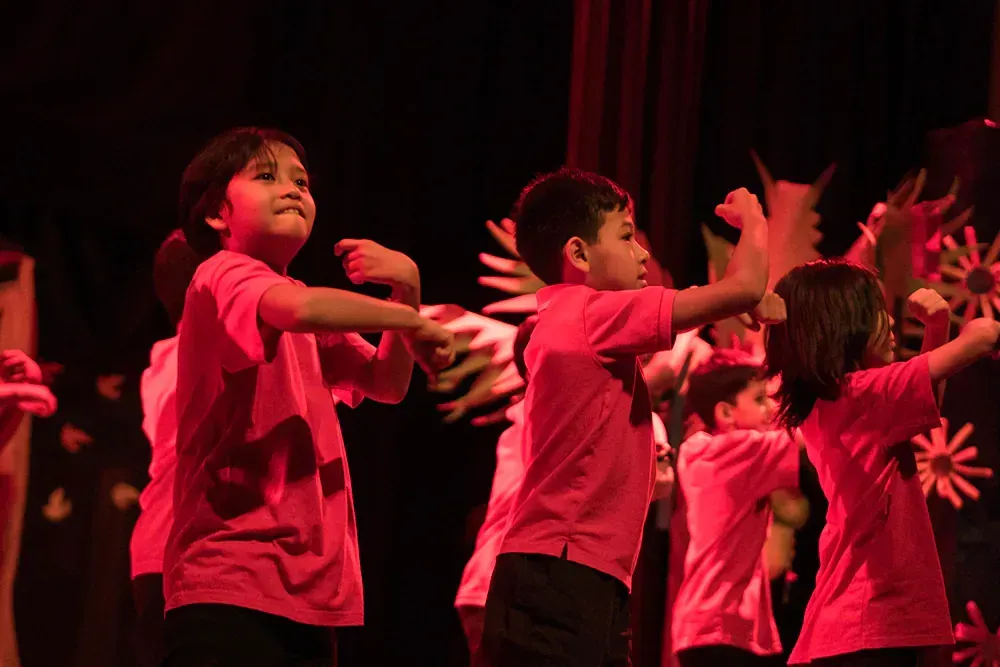 A group of children are dancing on a stage in red shirts.