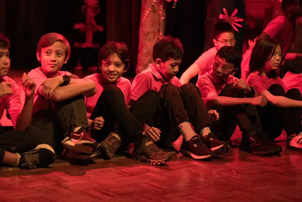 A group of children are sitting on the floor in a dark room.