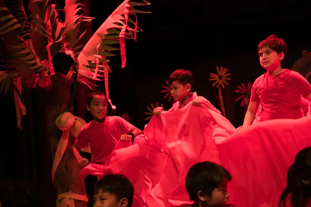 A group of children are dancing on a stage in red clothes.