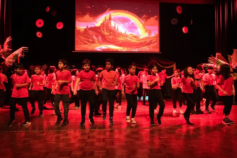 A group of children are dancing on a stage in front of a large screen.
